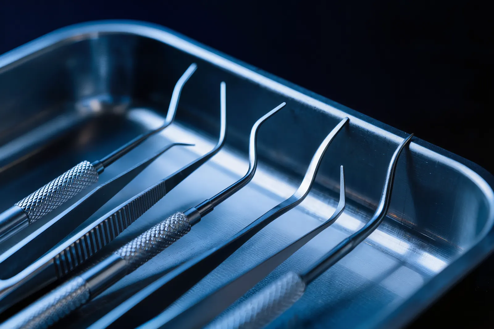Dental instruments arranged on a steel tray in cool blue light